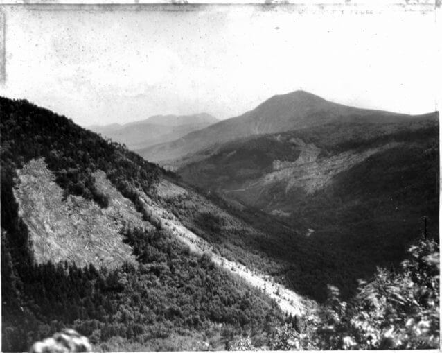 A 1910 photograph of the Pemigewasset Wilderness showing steep mountainsides stripped bare by logging, with clearcut slopes and distant ridgelines under a hazy sky.